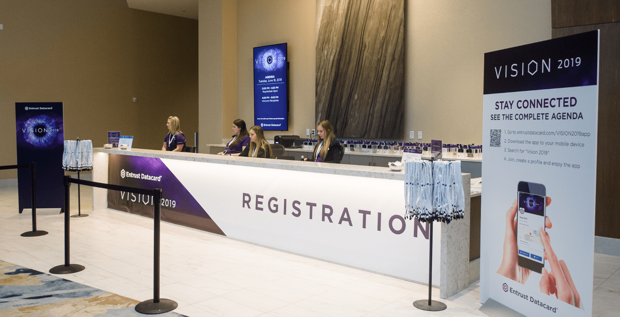 Large white and purple branded registration desk with stands holding lanyards for attendees. Custom signs explaining the event and presenting the theme of the event which is Vision 2019.