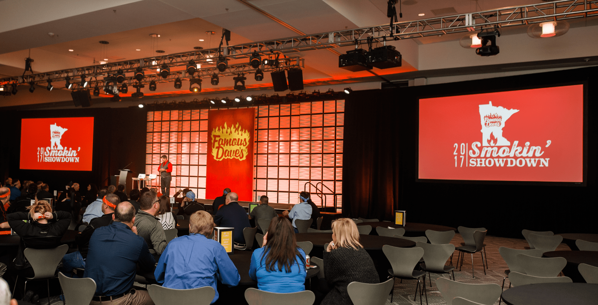 Keynote speaker standing in front of custom branded stage set presenting to a room full of Famous Dave's corporate employees at a kick-off event.
