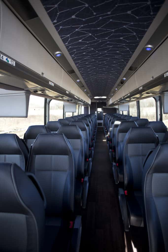 SASBus_14 - metroConnections Interior of a modern bus with blue seats, overhead racks, and a patterned ceiling, seen from the back toward the front.