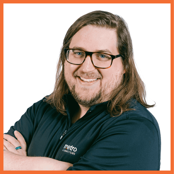 Smiling man with long hair and glasses, arms crossed, wearing a navy Metro Connections polo.