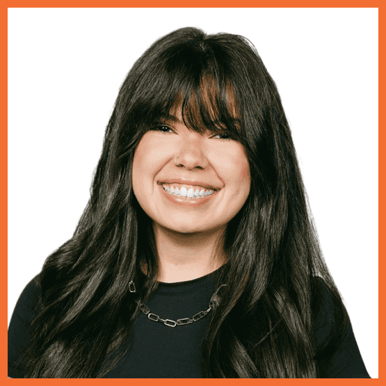 Smiling portrait of a woman with long dark hair and bangs, wearing a black top and a chain necklace against a white background.