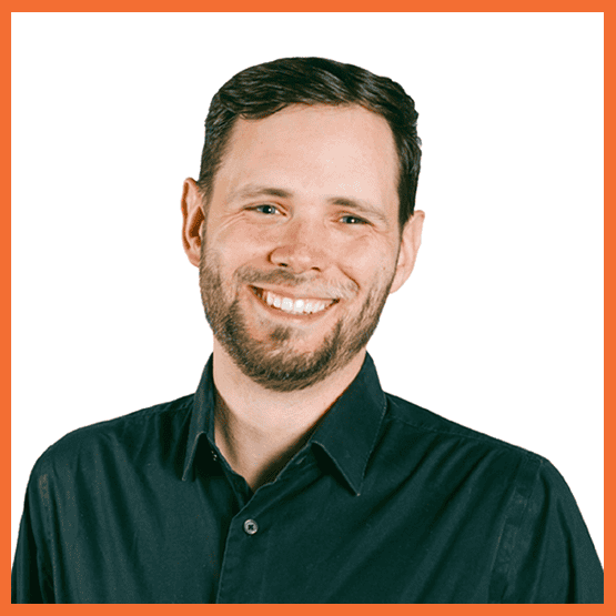 Tom_Hays_Quote - metroConnections Portrait of a smiling man with short dark hair and a beard, wearing a black button-down shirt, against a white background with an orange border.