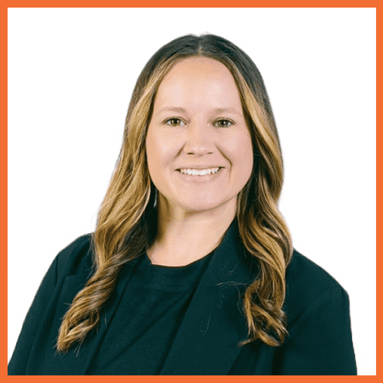 Smiling woman with long wavy hair in a dark blazer, posing for a professional headshot against a white background.
